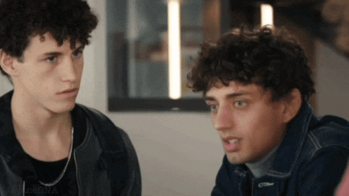 two young men with curly hair are sitting next to each other in a room with the word dna on the bottom