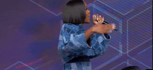 a woman in a blue plaid shirt is singing into a microphone with the word break written on the screen .