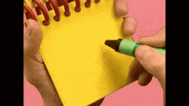 a person is holding a yellow notepad and a green crayon