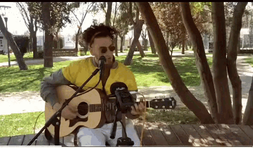 a man singing into a microphone while playing a guitar in a park