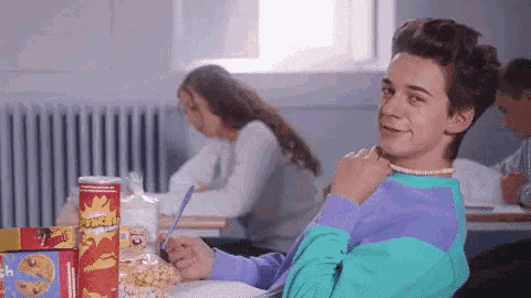 a boy is sitting at a desk with a box of crunchy peanut butter in front of him