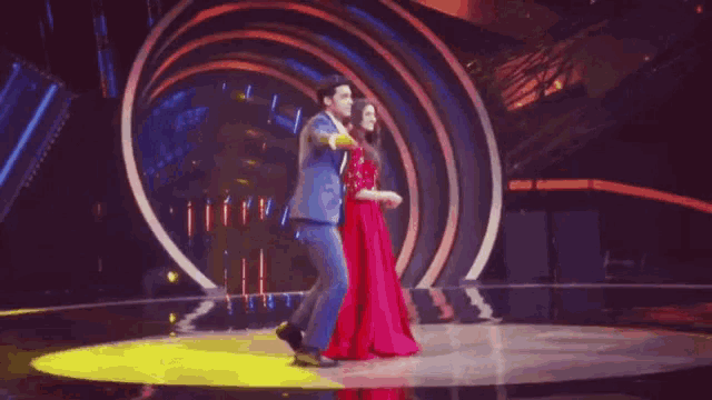 a man and a woman are dancing on a stage . the woman is wearing a red dress .