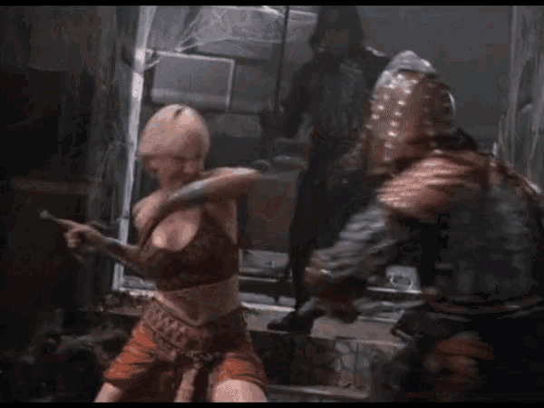 a woman with blonde hair is standing next to a man with a sword in a dark room .