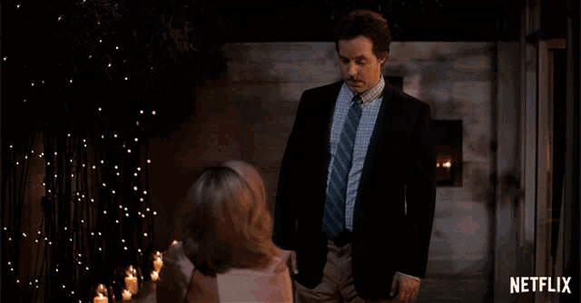 a man in a suit and tie is talking to a woman in front of a fireplace with netflix written on the bottom right