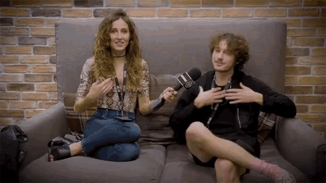 a man and a woman are sitting on a couch with a microphone between them