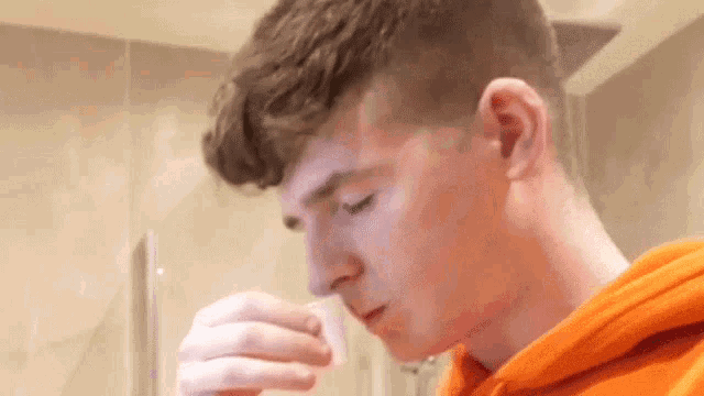 a young man in an orange hoodie is taking a pill from a bottle in his mouth .