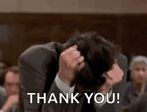 a man in a suit is holding his head and saying `` thank you '' in front of a group of people .