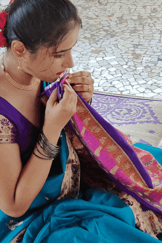 a woman in a blue and purple dress is sewing a piece of cloth