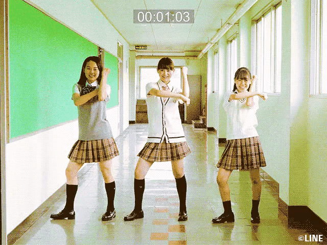 three girls in school uniforms are dancing in a hallway with a timer that says 00 01 03