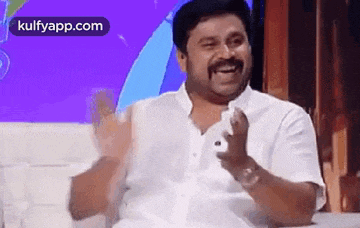 a man in a white shirt is sitting on a couch laughing .