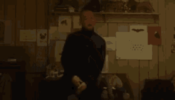 a blurry picture of a man standing in a room with a shelf full of drawings .