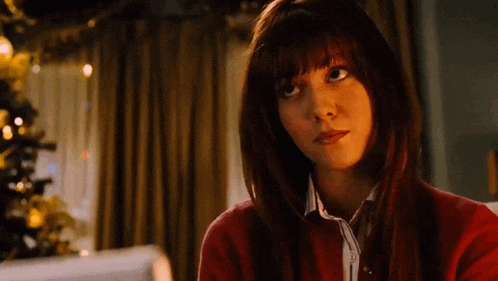 a woman with red hair and bangs is wearing a red sweater and looking up .