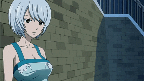 a woman with white hair and a blue dress stands in front of a brick wall