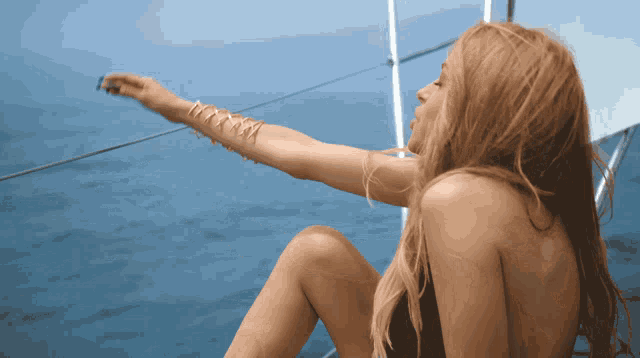 a woman in a black bikini sits on a sailboat in the ocean