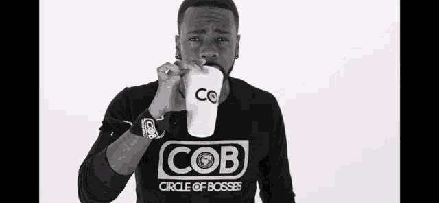 a man wearing a cob circle of bosses shirt drinks from a white cup