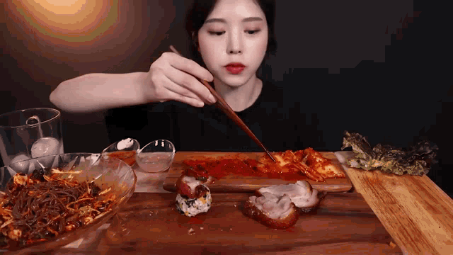 a woman is eating food with chopsticks on a wooden cutting board