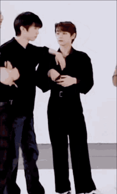two young men are standing next to each other in a room . one of the men is hugging the other .