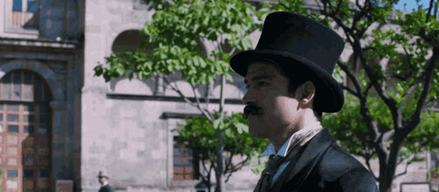 a man with a mustache wearing a top hat stands in front of a building