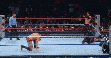 a wrestler is kneeling in the middle of a wrestling ring while a referee watches
