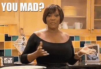 a woman in a black dress is standing in a kitchen and making a funny face .