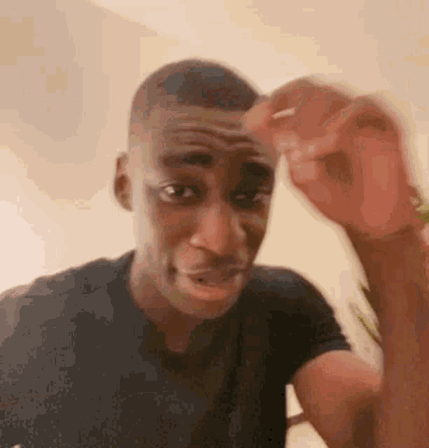 a man in a black shirt is making a funny face while holding his hand to his forehead .