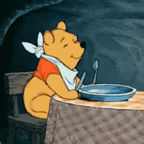 winnie the pooh is sitting at a table with a plate and spoon .