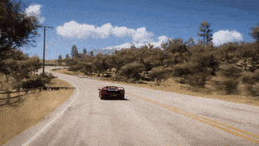 a red car is driving down a road with trees on both sides