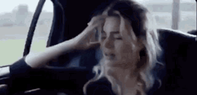 a woman is sitting in the back seat of a car with her head in her hand .