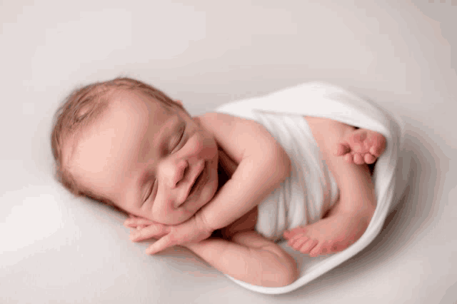 a baby wrapped in a white blanket smiles while sleeping