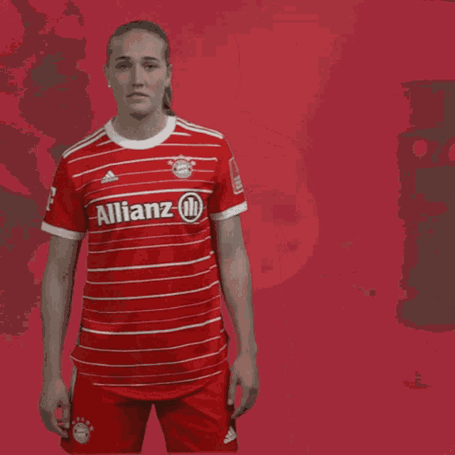 a woman wearing a red allianz shirt stands in front of a red background