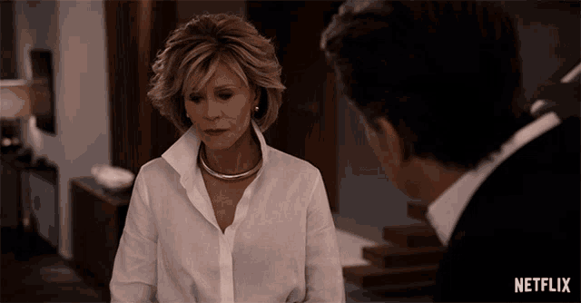 a woman in a white shirt is talking to a man in a black suit with a netflix logo behind her
