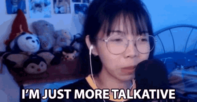 a woman wearing glasses and ear buds is talking into a microphone while sitting in front of a bed .