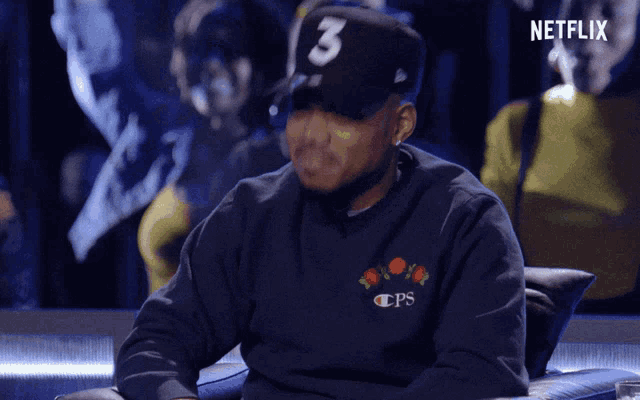 a man wearing a hat with the number 3 on it sits in a chair