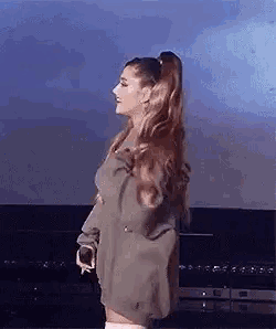 ariana grande is wearing a sweater dress and knee high socks while standing on a stage .