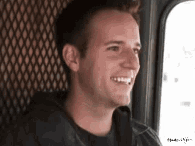 a man is smiling while looking out of a window behind a fence .