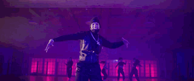 a group of people are dancing in a room with purple lights and smoke coming out of the ceiling .