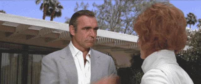 a man in a suit and white shirt talks to a woman with red hair