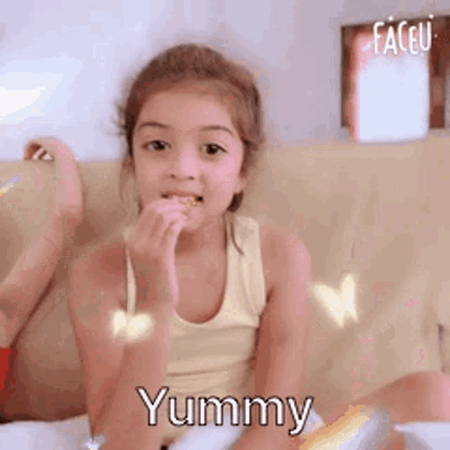 a little girl is sitting on a couch eating a candy bar and saying yummy .