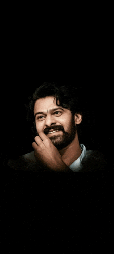 a man with a beard is smiling and covering his mouth with his hand