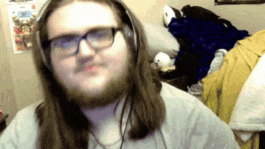 a man with long hair and glasses wearing headphones looks at the camera