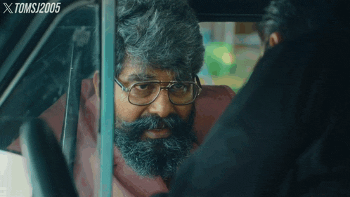 a man with glasses and a beard is looking out of a car window with xtomsj2005 written above him