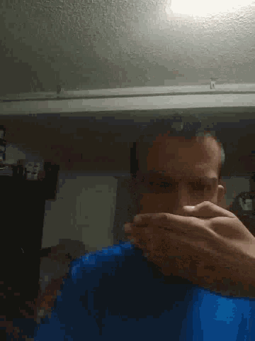 a man in a blue shirt is covering his face with his hands in a room .