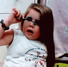a little girl is applying mascara to her face and wearing a shirt that says g.e.