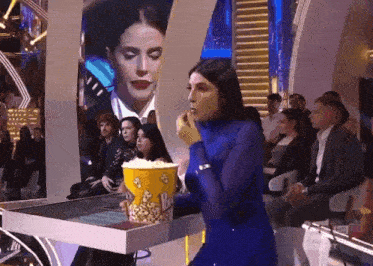 a woman in a blue dress is eating popcorn