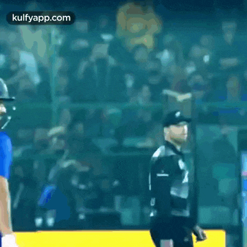 a cricket player wearing a helmet is standing next to another player .