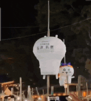 a white balloon with a cat on it is flying in the air at night .
