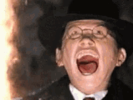 a man in a top hat and glasses is screaming in front of a fire