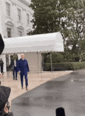 a man in a blue suit walking in front of a white house
