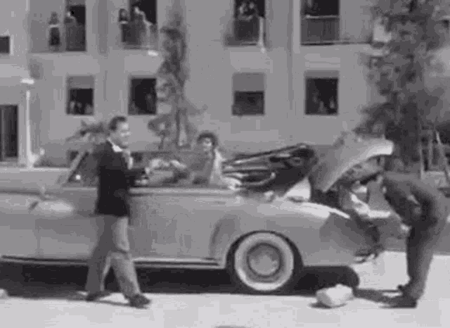 a man is opening the trunk of a car while a woman sits in the back seat .