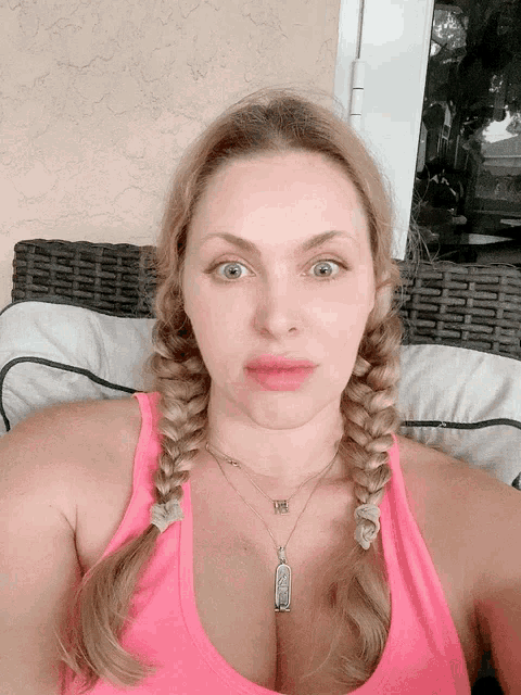 a woman wearing a pink tank top and a necklace with a pendant that says ' i love you ' on it